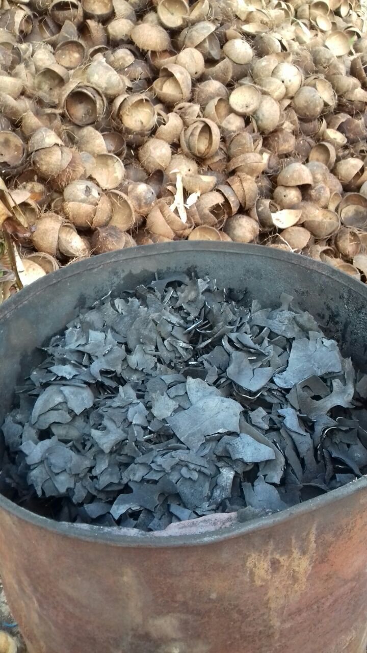 Charcoal in drum with pile of raw coconut shells