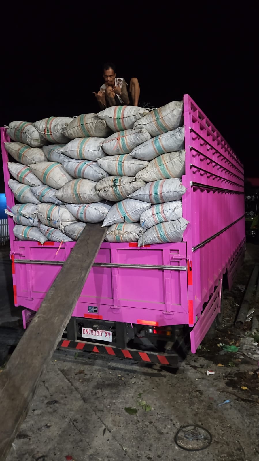 Pink truck body fully loaded with striped woven sacks at night